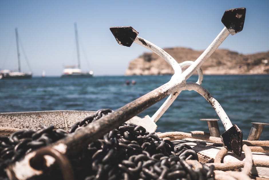 Close-up of boat anchor and chains with ocean and sailboats in the background.